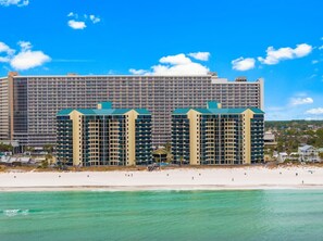 Ein großes Hotel mit mehreren Etagen und Balkonen, in Strandnähe mit klarem, türkisblauem Wasser.