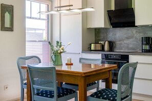 Una cocina moderna con una mesa de madera, sillas azules, un jarrón verde con flores, un tostador, un hervidor y una cafetera.
