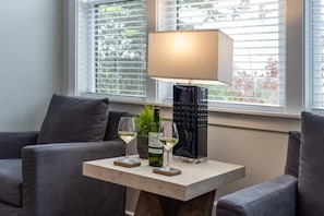 A modern living room with a sofa, a coffee table, a lamp, and two glasses of white wine.