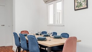 Et spiseområde med et træbord, blå og lyserøde stole og et vindue med gardin.