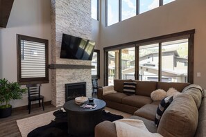 A living room with a stone fireplace, a large flat-screen TV mounted on the wall, a brown sectional sofa, and a round coffee table.