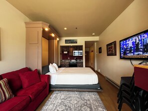 Ein Hotelzimmer mit Bett, einem roten Sofa, einem Fernseher, einer Küchenzeile und einem Badezimmer.