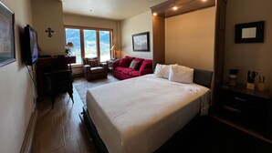 A bedroom with a large bed, a desk, a chair, a red sofa, and a TV mounted on the wall. - Cozy Studio for 2 with Mountain Views in Purgatory Village - Kendall 342 (Durango)