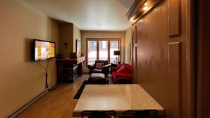 A living room with a TV, a fireplace, a dining table, and a red sofa. - Studio for 2 at Purgatory Resort in the main plaza buildings (Durango)
