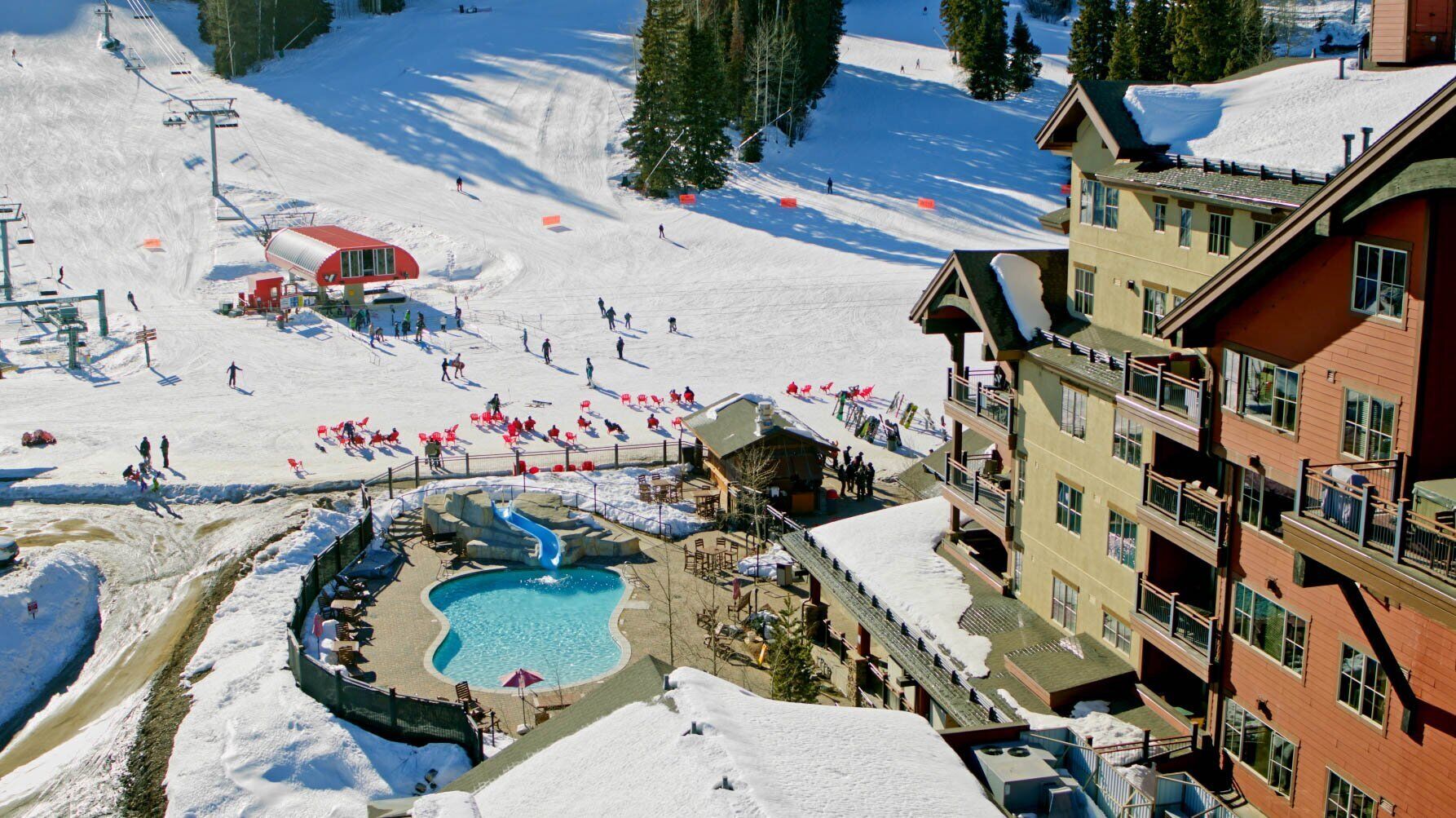 A ski resort with a pool area, ski lifts, and a building with balconies.