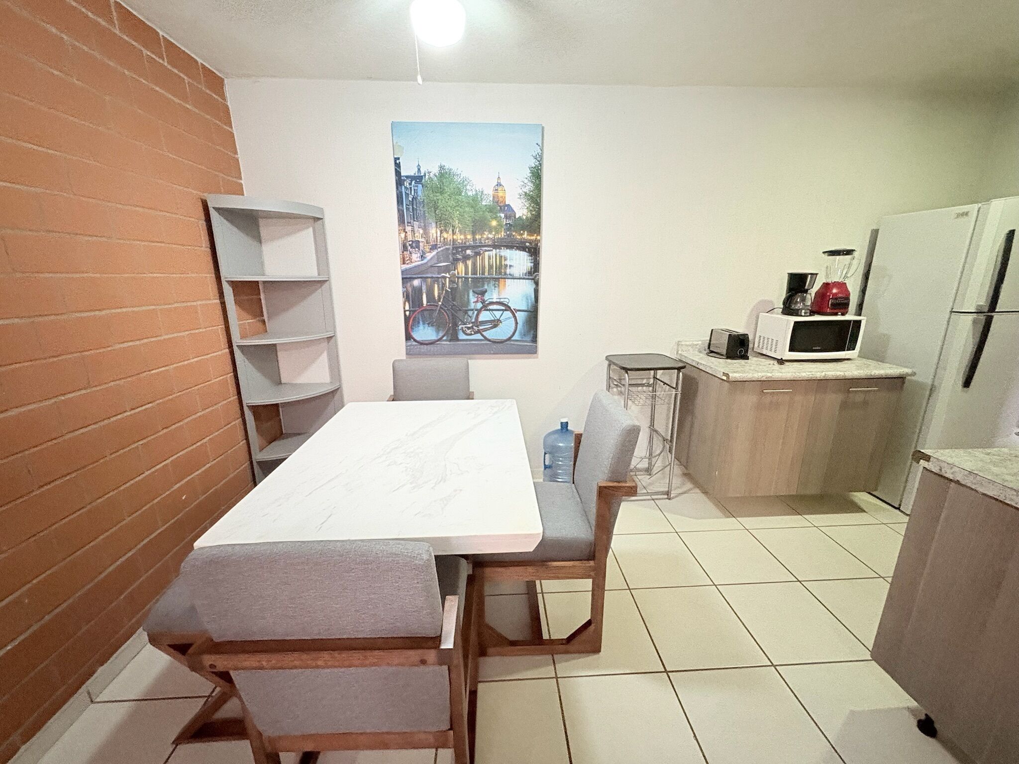 A compact kitchen with a dining table and chairs, a water dispenser, a microwave, and a refrigerator.