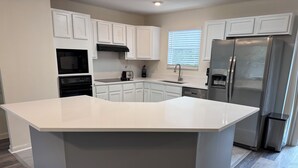 Una cocina moderna con armarios blancos, una isla grande, electrodomésticos de acero inoxidable y un suelo de madera en patrón de espiga.