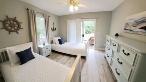 Un dormitorio con dos camas, un aparador, un ventilador de techo y vistas al exterior.