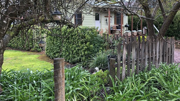 Ein Garten mit Holzzaun, Vogelhaus und einem Haus im Hintergrund.