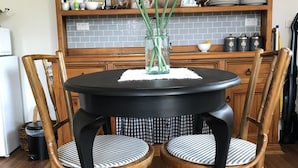 Ein Esstisch mit zwei Stühlen, eine Vase mit Blumen und eine Holzkommode im Hintergrund.