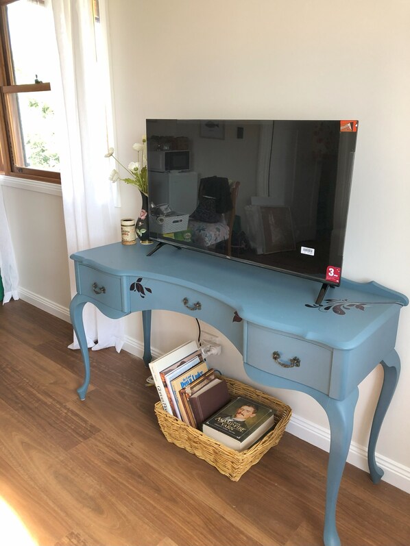 Una scrivania blu con una televisione a schermo piatto, un cesto di vimini sotto e una finestra con tende.