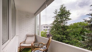 Un balcón con un muro de ladrillo blanco, dos sillas de mimbre y un pequeño parche de césped artificial.