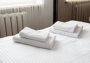 A neatly made bed with white towels folded on top, a radiator, and a window with blinds. - Embassy Avenue At Royal Park (Warszawa)