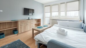 A modern bedroom with a bed, a TV, a desk, and a window with blinds.