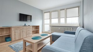 A modern living room with a grey sofa, wooden coffee table, and a TV mounted on the wall.
