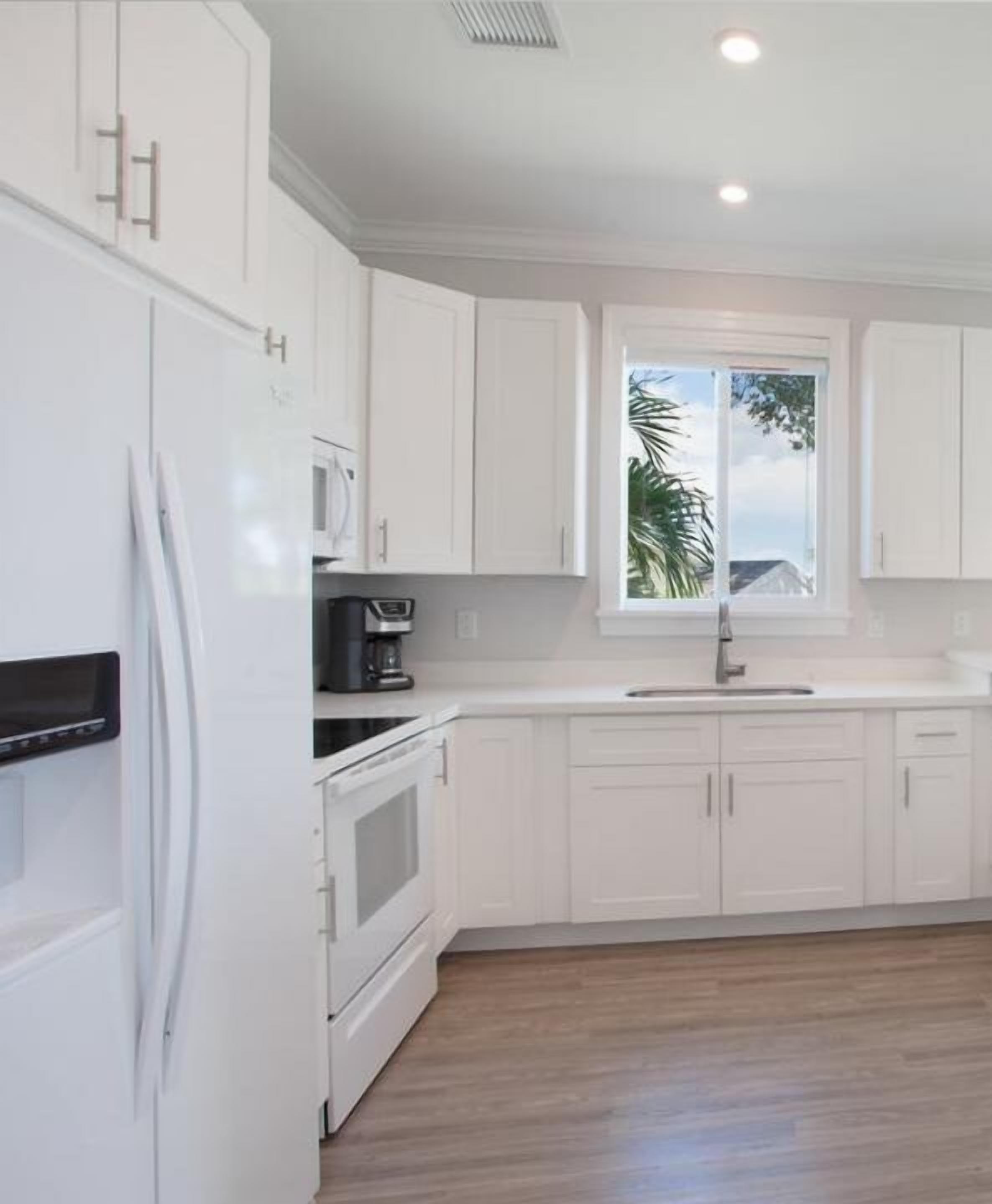 A modern kitchen with white cabinetry, a built-in oven, a microwave, and a sink under a window.
