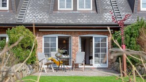 A house with a brick exterior, a tiled roof, and a front door leading to a covered patio area with outdoor furniture. - Weetstich - Willkommen im Weetstich in Archsum (Archsum)