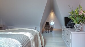 A bedroom with a sloped ceiling, a bed, a dresser, a television, and a window with a view of sheep. - Weetstich - Willkommen im Weetstich in Archsum (Archsum)