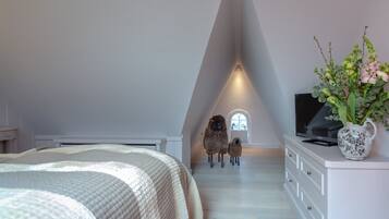 Ein Schlafzimmer mit schrägen Wänden, einem Bett, einer Kommode, einem Fernseher und einem Fenster mit Blick auf Schafe.