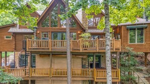 A multi-story log cabin with wooden balconies and a stone foundation. - Kind Oak Lake House Peaceful Lakeside Cabin with Hot Tub & Private Dock in Mill Springs (Mill Spring)