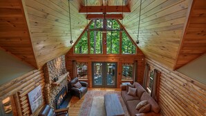 A log cabin interior with a stone fireplace, wooden walls, a large window, and a cozy seating area. - Kind Oak Lake House Peaceful Lakeside Cabin with Hot Tub & Private Dock in Mill Springs (Mill Spring)