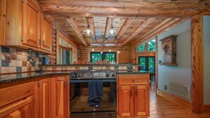 A spacious kitchen with wooden cabinets, a central island, and a large stove. - Kind Oak Lake House Peaceful Lakeside Cabin with Hot Tub & Private Dock in Mill Springs (Mill Spring)