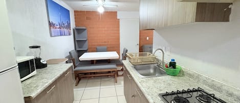 Eine kompakte Küche mit Gasherd, Spüle, Mikrowelle, Mixer und einer Essecke mit Tisch und Stühlen.