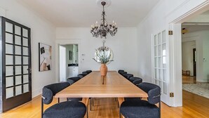 Ein geräumiger Essraum mit einem langen Holztisch, dunklen gepolsterten Stühlen, einer großen Vase mit Grünpflanzen und einer Kristallleuchter.