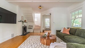 Ein geräumiges Wohnzimmer mit Holzboden, einem grünen Sofa, einem Couchtisch und einem Kamin.