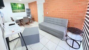A compact living space with a grey sofa, a small round table, a white desk with papers, a TV on the wall, and a brick accent wall. - Torre Federacion 602 Zona Centro Guadalajara (Guadalajara)