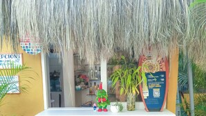 A small outdoor bar area with a thatched roof, two wooden stools, and a variety of plants around. - Aloha Lina (Máncora)