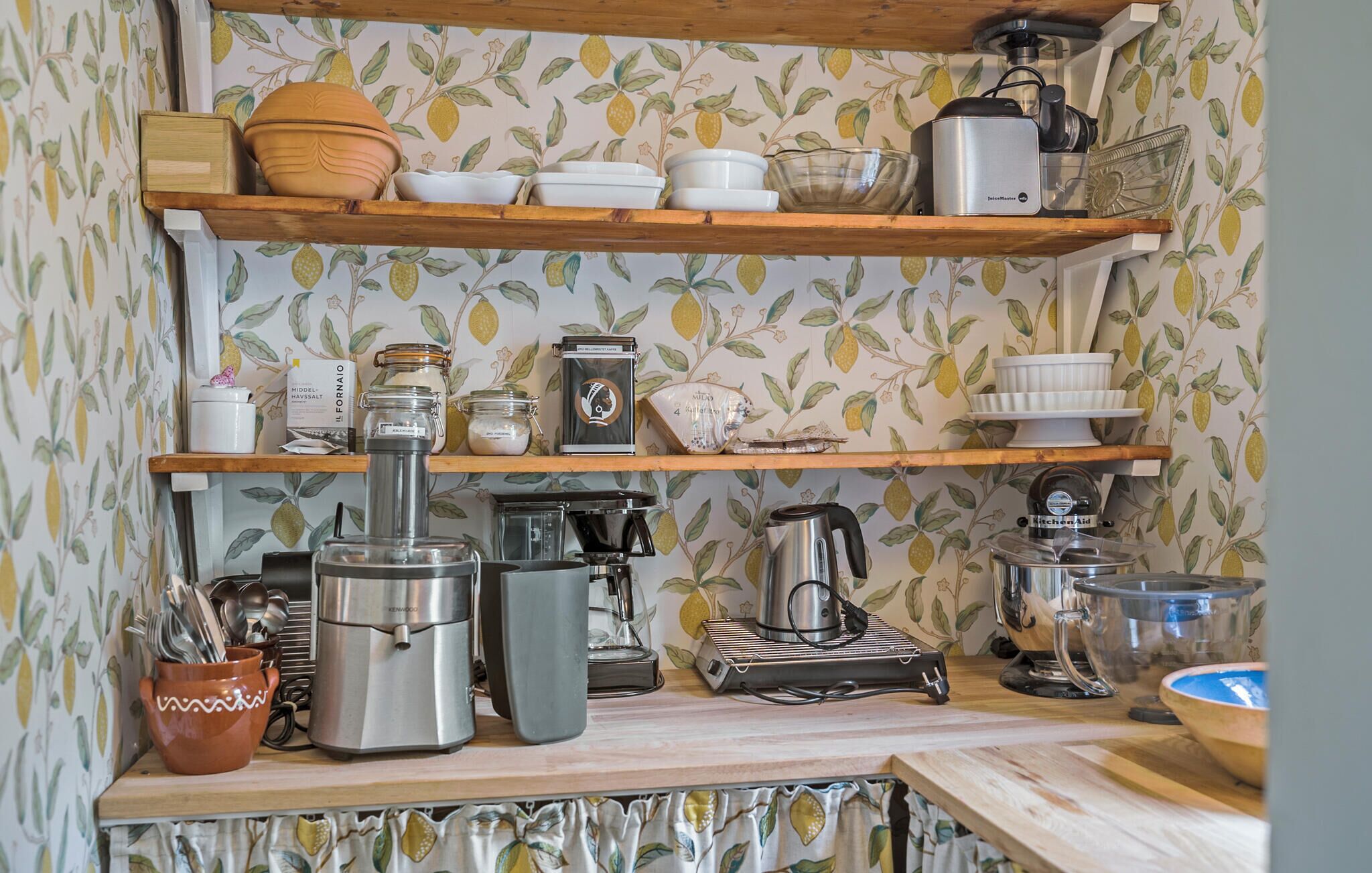 A kitchen with wooden shelves holding various kitchenware and appliances, including a coffee maker, a kettle, and a blender.