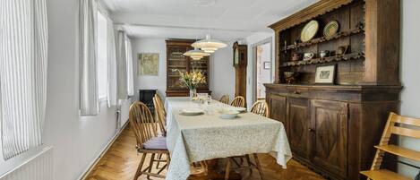 A dining room with a long table, wooden chairs, a cabinet with dishes, and a hanging light fixture.