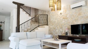 A living room with a stone wall, a white sofa, a white coffee table, a TV, and a staircase with a wooden railing. - Lovely home in Smoljanci (Smoljanci)
