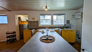 A kitchen with a long island, yellow cabinets, a window with blinds, and a hanging light fixture. - De Lütte Seileree - de Lütte Seileree - Ein Sicherer Hafen und Rückzugsort für Hund und Mensch (Heringsdorf)
