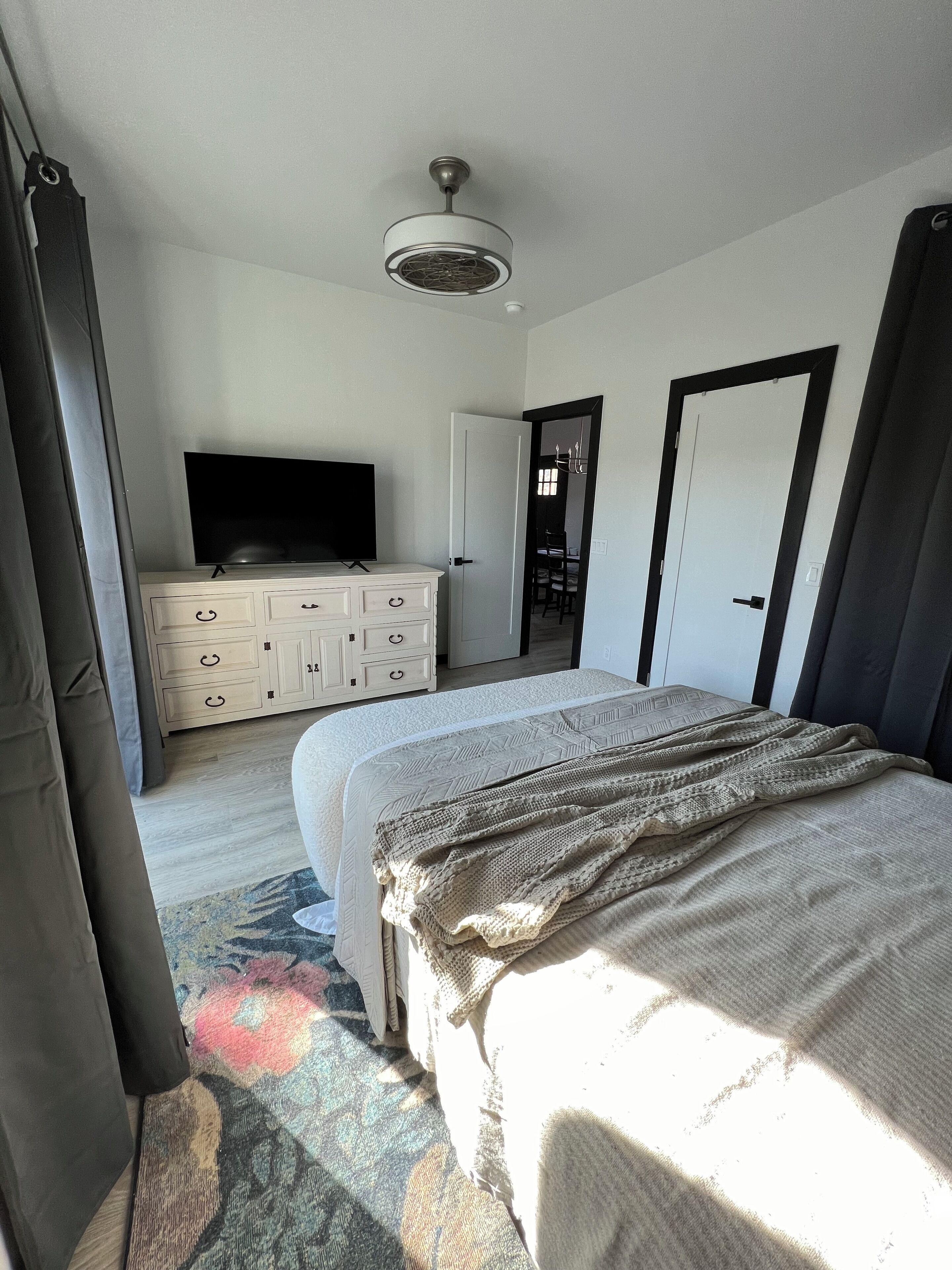 A bedroom with a bed, a dresser, a television, and a ceiling fan.