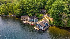 A lakeside cabin complex with docked boats, surrounded by dense forest. - Dockside Dream | 4 mins to Mt Sunapee | Dock | VIEWS | Grill (Newbury)