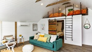 A loft-style room with a green sofa, a ladder, and a loft bed with a red blanket. - Dockside Dream | 4 mins to Mt Sunapee | Dock | VIEWS | Grill (Newbury)
