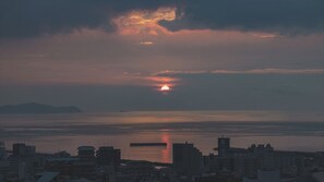 Un paisaje urbano al atardecer con un mar tranquilo y montañas lejanas.