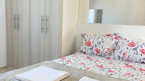 A bedroom with a bed, two towels, a floral-patterned bedspread, and a wardrobe. - Pérola do Aquarius IV (São José dos Campos)