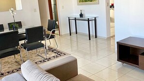 A modern living room with a sofa, a dining area with chairs, a small table, and a painting on the wall. - Pérola do Aquarius IV (São José dos Campos)