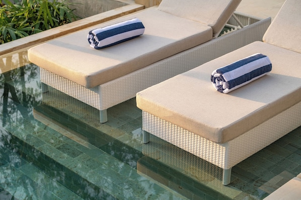 Two lounge chairs with towels, positioned by a poolside.