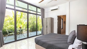 Ein Schlafzimmer mit einem großen Bett, Blick auf einen Garten durch eine Schiebetür und einer modernen Klimaanlage.