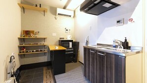 Eine kompakte Küche mit Mikrowelle, Herd und Spüle. Holzregale und eine kleine Arbeitsplatte sind vorhanden.