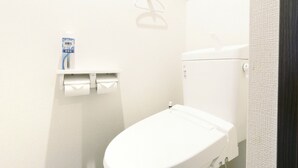 Eine weiße Toilette mit einem Papierhandtuchspender und einer Toilettenpapierrolle an einem Wandhalter.