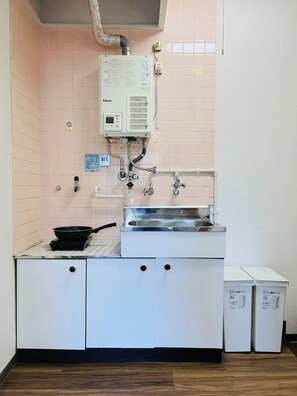A kitchen with pink tiled walls, a white sink, a stove, and a water heater. - Kokoro no Sato  Lotus Room 201 - Room 201 / Kyoto Kyōto (Kyoto)