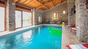 A swimming pool with stone walls and wooden beams, surrounded by lounge chairs and a view of greenery outside. - Amazing home in Privas with sauna (Privas)