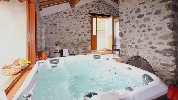 A stone-walled bathroom with a hot tub, wooden beams, and a view of the outdoors. - Amazing home in Privas with sauna (Privas)