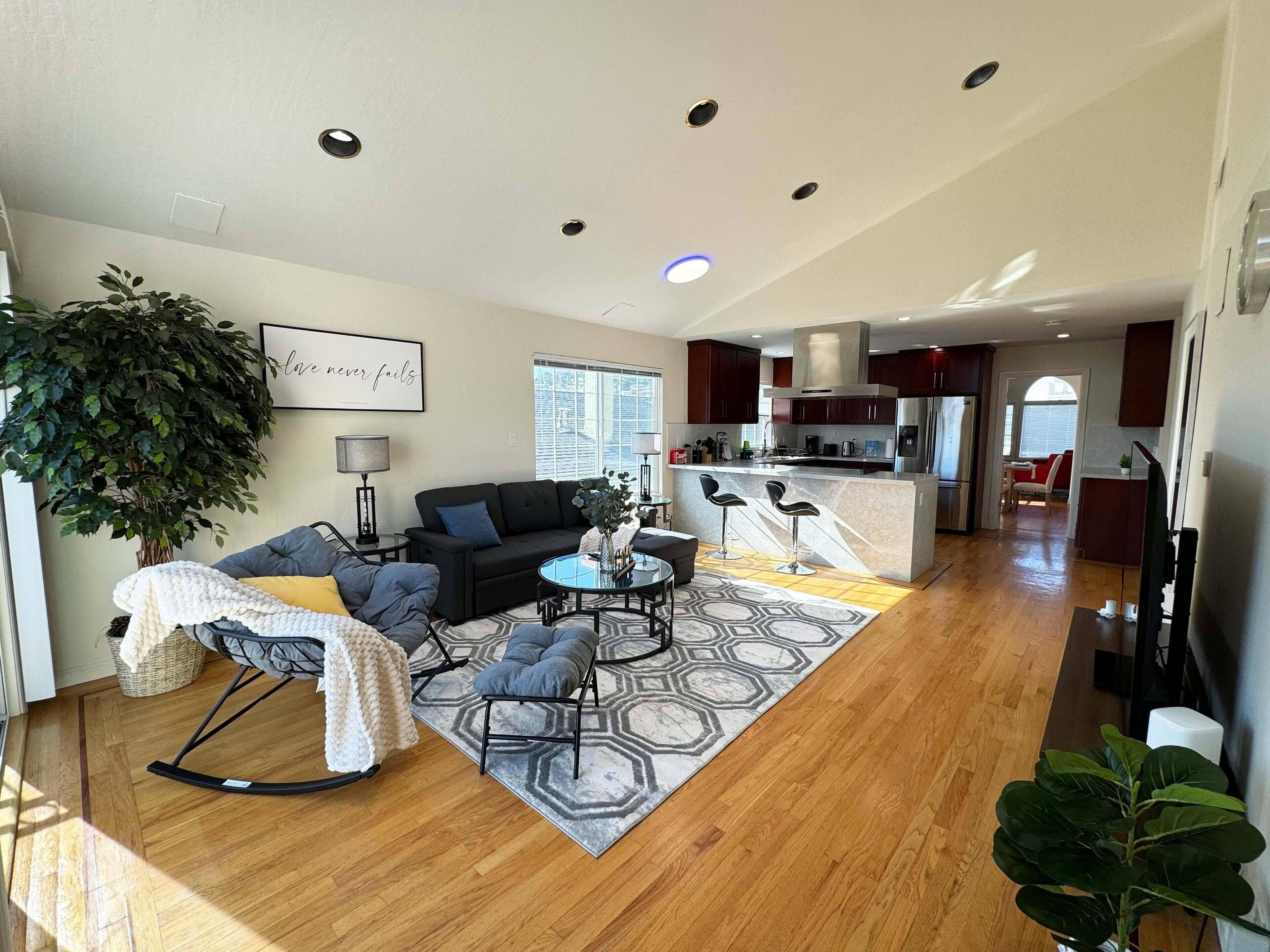 Un salon moderne comprenant un canapé, des fauteuils, une table basse et un tapis. Il y a également un coin cuisine avec un réfrigérateur, une cuisinière et des placards.