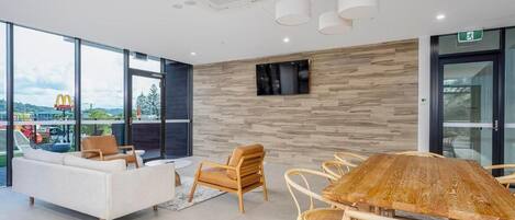 Una sala de reuniones moderna con una mesa grande, asientos cómodos, un televisor montado y ventanas amplias que ofrecen vistas al exterior.